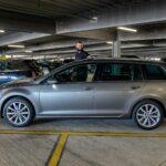 Man standing by a silver station wagon in parking garage