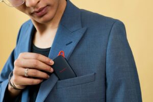 Hand inserting a black electronic device into a blazer pocket.