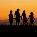 A family in silhouette holding hands against a warm orange sky by the sea